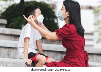 Mom Is Wearing A Medical Mask For Her Child. Little Asian Boy And Mom In Medical Mask. Asian Family Protection Virus Concept.