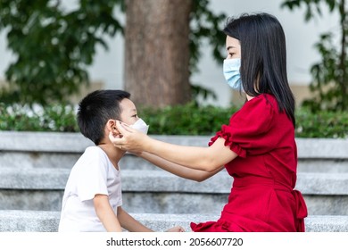 Mom Is Wearing A Medical Mask For Her Child. Little Asian Boy And Mom In Medical Mask. Asian Family Protection Virus Concept.