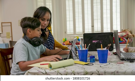 A Mom Working From Home And Sharing A Small Space With Her Children Who Are Attending School Via Virtual Classrooms Stops To Help Her Son.