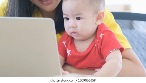 Mom Is Working On A Laptop And Raising Her Baby At The Same Time In The Office. Mother Holding Baby Infant And Using Computer Laptop Facetime Video Call To Father.