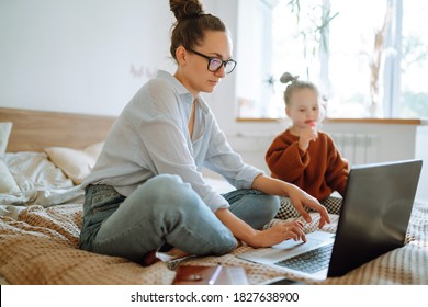 Mom Working Remotely On Laptop While Taking Care Of Her Baby. Young Mother On Maternity Leave Trying To Freelance  With Daughter. Stay At Home. Covid-19.