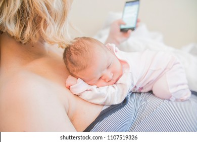 mom works on the phone and holds a newborn baby