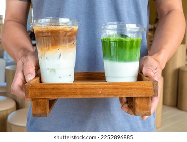 A moment of relaxation—man holding an ice latte coffee and matcha latte on a wooden tray, capturing a calm and indulgent experience. - Powered by Shutterstock