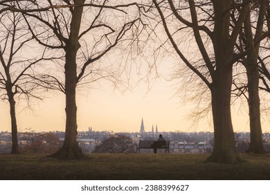 Moment of solitude as a distant figure sits on a quiet park bench during a cold winter sunset or sunrise at Inverleith Park in Edinburgh, Scotland, UK. - Powered by Shutterstock