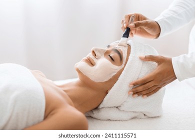 In a moment of tranquility, young indian woman experiences the luxury of a professional facial mask treatment, enhancing her skin's radiance. Day at spa, beauty treatment - Powered by Shutterstock