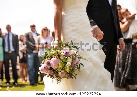 Moment in wedding,  bride and bridegroom holding hands with bouquet and wedding guests in background