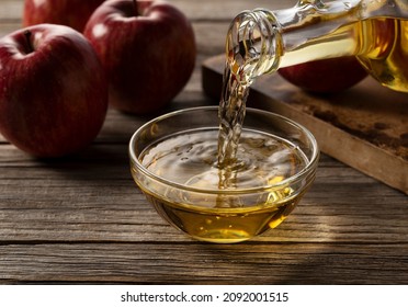 The moment you pour apple cider vinegar in a glass container against a wooden background.