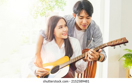 Moment young asian couple having fun with guitar at home teaching acoustic guitar romantic : Handsome boyfriend teaches his girlfriend easy guitar chords with love.