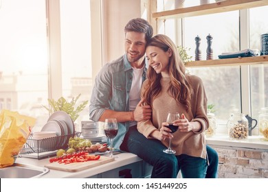 Moments Of Intimacy. Beautiful Young Couple Cooking Dinner And Drinking Wine While Standing In The Kitchen At Home