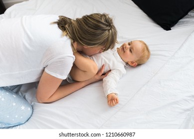 Mommy And Baby Playing On Bed In The Morning, Mommy Cuddling Her Baby And Kissing Her Tummy.