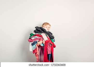 Mommy Little Helper. Cute Caucasian Girl Sorting Clothes. Adorable Funny Child Arranging Organazing Clothing. Kid Holding Messy Stack Pile Of Clothes Things. Home Chores Housework.