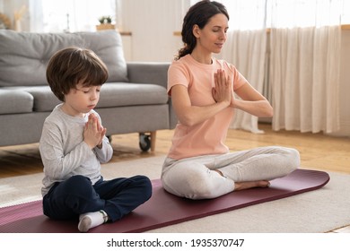 Mommy Practicing, Teaching Child To Meditate. Fit Mom With Little Son Doing Yoga Exercise Sit On Yoga Mat On Floor At Home. Calm Mother And Kid Sitting In Lotus Pose. Stress Relieve, Wellness Concept.