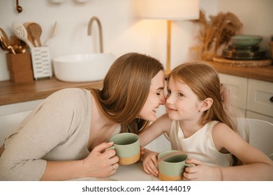 Mommy touches noses child. Mother hugs children and spend time together. Family communication of mom and kid. Happy mother with daughter drinking tea or cocoa sitting in kitchen and having fun. - Powered by Shutterstock