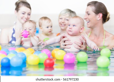 Moms and children at infant swimming lesson playing with balls