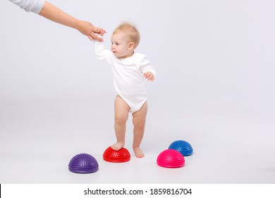 Mom's Hand Holding Baby Girl In White Bodysuit With Physiotherapy Tools For Flat Feet-balance Pod On White Background