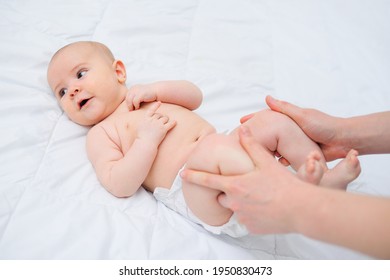 Mom's Hands Hold The Baby's Legs At His Tummy. Massage A Newborn Baby Against Bloating And Colic.