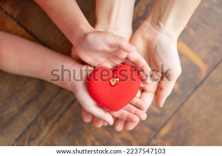 mom's hands hold the baby's hands and a red heart inside on a wooden brown background, the concept of Valentine's Day or mother's day
