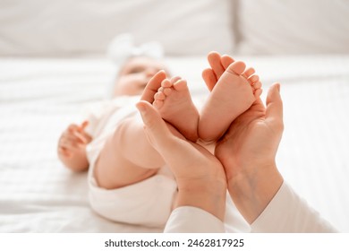 mom's hands hold the legs of a small child on a white background on the bed, a place for text, the baby's heels in parental hands. - Powered by Shutterstock