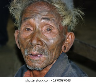 Mon district, Nagaland, India - 03 02 2009 : Closeup portrait of old Naga Konyak tribe head hunter warrior with traditional facial tattoo on dark background