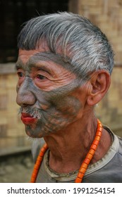 Mon district, Nagaland, India - 03 09 2014 : Closeup three quarter outdoor portrait of old Naga Konyak tribe head hunter warrior with traditional facial tattoo and orange coral necklace chewing betel