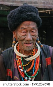Mon district, Nagaland, India - 03 09 2014 : Closeup front portrait of old Naga Konyak tribe head hunter warrior with traditional facial tattoo, spectacular horn earrings and boar tusk necklace 