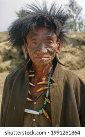 Mon district, Nagaland, India - 03 10 2014 : Closeup front portrait of old Naga Konyak tribe head hunter warrior with traditional facial tattoo, fur hat, horn earrings and boar tusk necklace 