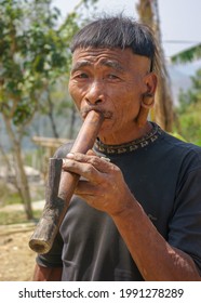 Mon district, Nagaland, India - 03 10 2014 : Outdoor portrait of middle aged Naga Konyak tribe man with typical hair style smoking traditional bamboo water pipe