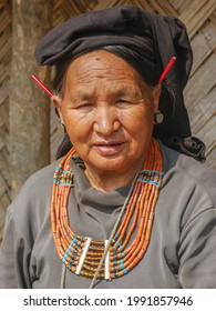 Mon district, Nagaland, India - 03 11 2014 : Outdoor front portrait of aging Naga Konyak tribal woman wearing beautiful traditional necklace and red porcupine quills in her ears indicating her status