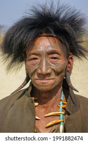 Mon district, Nagaland, India - 03 10 2014 : Closeup front portrait of smiling old Naga Konyak tribe head hunter warrior with traditional facial tattoo, fur hat, horn earrings and boar tusk necklace 