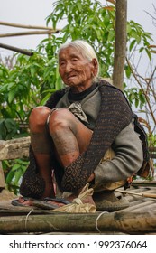 Mon district, Nagaland, India - 03 01 2009 : Very old Naga Konyak tribe woman with traditional leg tattoo sitting outdoor on bamboo terrace