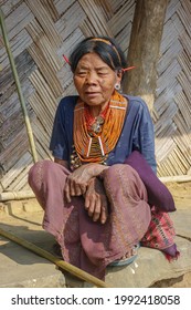 Mon district, Nagaland, India - 03 11 2014 : Outdoor full body front portrait of squatting old Naga Konyak tribal woman wearing traditional necklace and porcupine quills in her ears indicating status