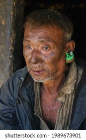 Mon district, Nagaland, India - 11 19 2010 : Closeup three quarter portrait of old Naga Konyak tribe man with big ear piercing holding tobacco bag on dark background