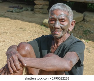 Mon district, Nagaland, India - 11 20 2010 : Closeup outdoor portrait of old Naga Konyak tribe head hunter warrior with traditional facial tattoo sitting on the ground