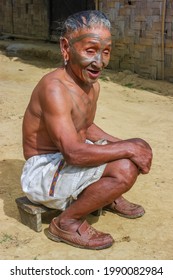 Mon district, Nagaland, India - 11 20 2010 : Outdoor portrait of smiling old Naga Konyak tribe head hunter warrior with traditional facial tattoo sitting on low wooden stool