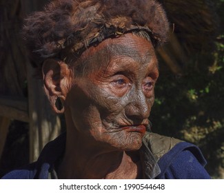 Mon district, Nagaland, India - 11 25 2013 : Close up three quarter outdoor portrait of old Naga Konyak tribe head hunter warrior with traditional facial tattoo wearing fur hat on natural background