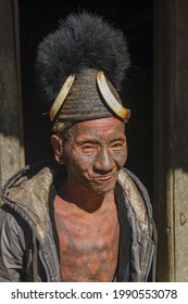 Mon district, Nagaland, India - 11 25 2013 : Isolated front portrait of old Naga tribe head hunter warrior with traditional facial and chest tattoo wearing Konyak hat on dark background