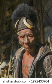 Mon district, Nagaland, India - 11 25 2013 : Front portrait of old Naga Konyak tribe head hunter warrior with traditional facial and chest tattoo wearing typical cane hat with boar tusks and bear fur