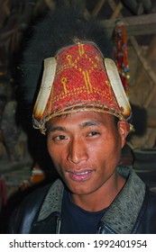 Mon, Nagaland, India - 03 02 2009 : Indoor close up portrait of handsome young Naga Konyak tribe man wearing beautiful traditional red bamboo and cane hat with boar tusks and bear fur