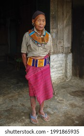 Mon, Nagaland, India - 03 03 2009 : 
Full length portrait of old Naga Konyak tribe woman standing and wearing traditional necklace, belt, earrings and black head scarf on dark background