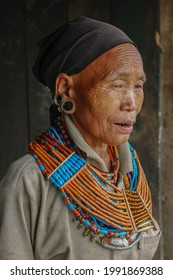 Mon, Nagaland, India - 03 03 2009 : 
Three quarter portrait of old Naga Konyak tribe woman wearing beautiful traditional necklace and earrings with black head scarf on dark background