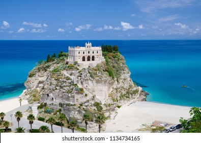 Monastery Sanctuary church of Santa Maria dell Isola on top of rock Tyrrhenian Sea and green palm trees, blue sky white clouds in summer clear day, Tropea town, Vibo Valentia, Calabria, Southern Italy