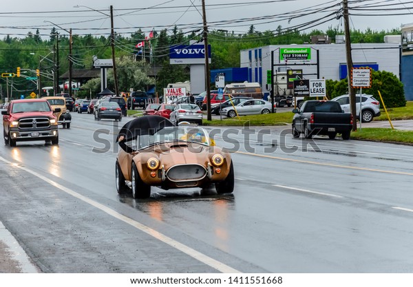 Moncton, New Brunswick, Canada - July 12, 2015 :\
Kit car based on a 1965 Ford Shelby Cobra gets caught in the rain\
leaving Centennial Park as the 2015 Atlantic Nationals Automotive\
Extravaganza closes