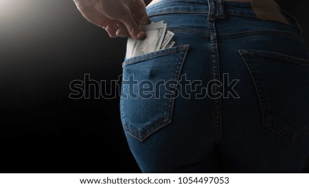 Money in the back pocket of the girl's jeans. On a black background, with an empty space for inscription or advertising.