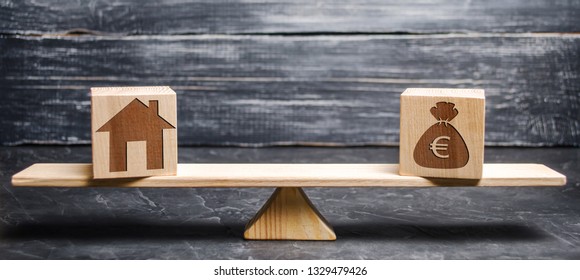 Money Bag With Euro Sign And Wooden House On Scales On Wooden Blocks. The Concept Of Real Estate Purchase. Sale Of Property. Payment Of The Mortgage. Redemption Of Taxes. Tax Refund. Apartment Loan