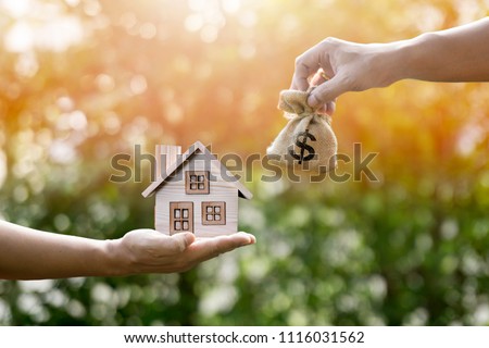 Money bag home and man hands in sunlight represent to exchange or saving money or investing to buy a home or loan to buy a house or real estate or investment for the future.