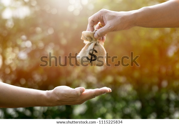 Money bag and man hand and giving in sunlight show\
giving savings or Loan to Buy Assets or give money to pay in the\
future or divide the investment for retirement or for the future\
Concept of money.