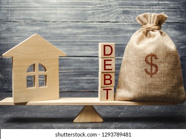 Money bag and wooden blocks with the word Debt and a miniature house on the scales. Payment of debt for real estate. Pay off the mortgage loan. Risks of buying a house. Buying an apartment on credit.