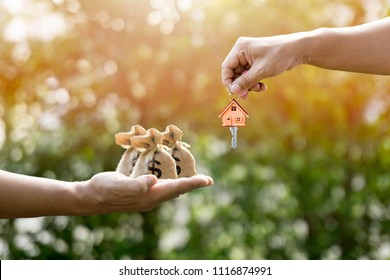 Money bags on hand and house key in hand and Sunlight represent Exchange or sell  or contract for renting a house or real estate. Saving money or investing to buy a home or loan. - Shutterstock ID 1116874991