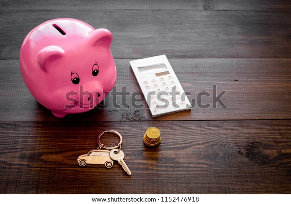 Money for buy car. Moneybox in shape of pig near\
keychain in shape of car, coins, calculator on dark wooden\
background copy space