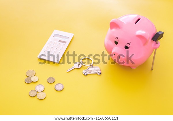 Money for buy car. Moneybox in shape of pig near\
keychain in shape of car, coins, calculator on yellow background\
copy space
